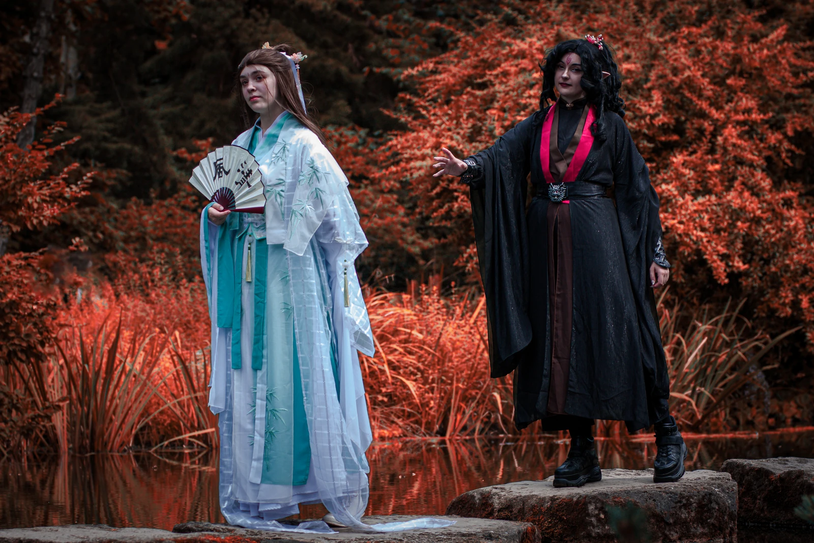 Zwei Cosplayer in hellen und dunklen Gewändern vor rotem Herbstlaub