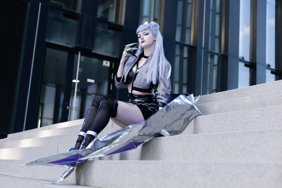 Cosplayerin mit silberviolettem Haar auf einer Treppe vor Glasfassade