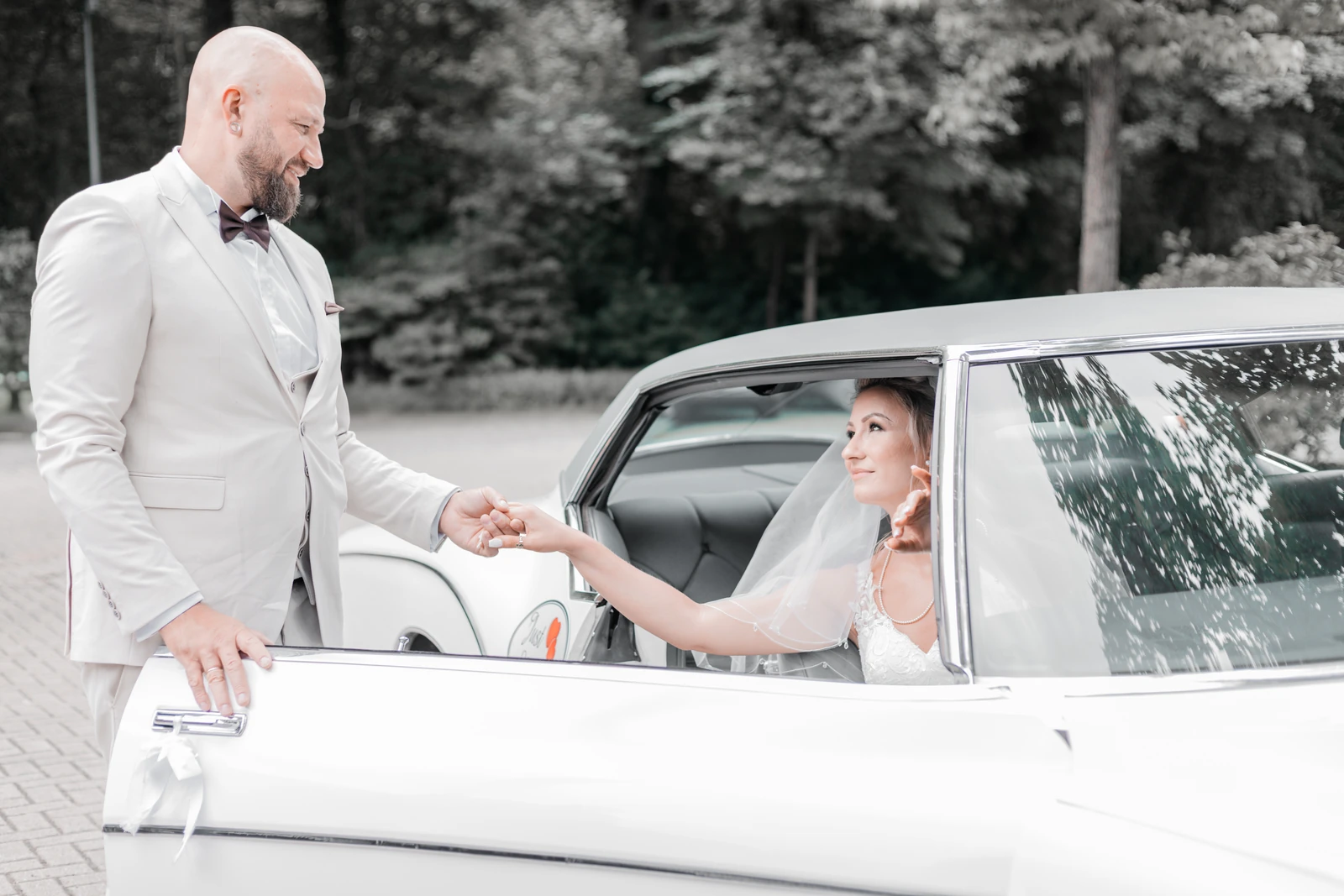 Bräutigam reicht der Braut am Hochzeitsauto die Hand